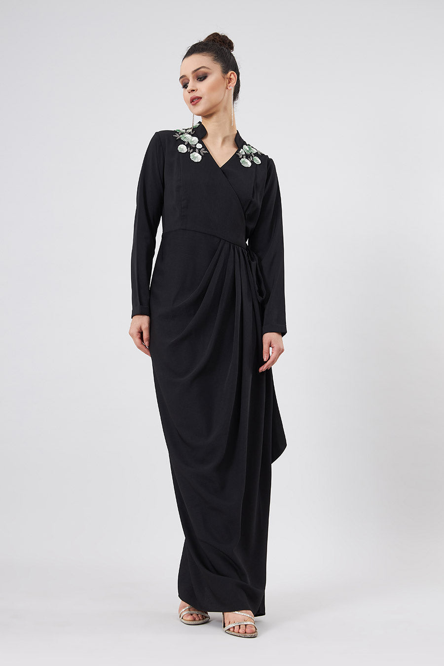 A woman standing and modeling a black floral lounge wrap dress with a V-neckline, full sleeves, and side tie-up detailing.