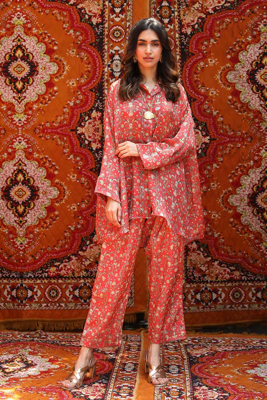 A woman modeling a red satin georgette blend shirt and pants co-ord set with a high-low hem and pleat detailing, paired with a matching drawstring waist.