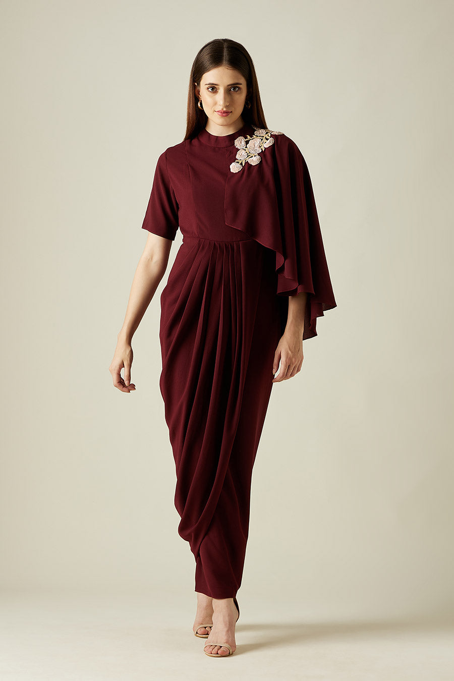 A woman standing and modeling a wine red, floral embroidered drape dress with a round neckline and back button closure. She is wearing a similar color and style of shoes.