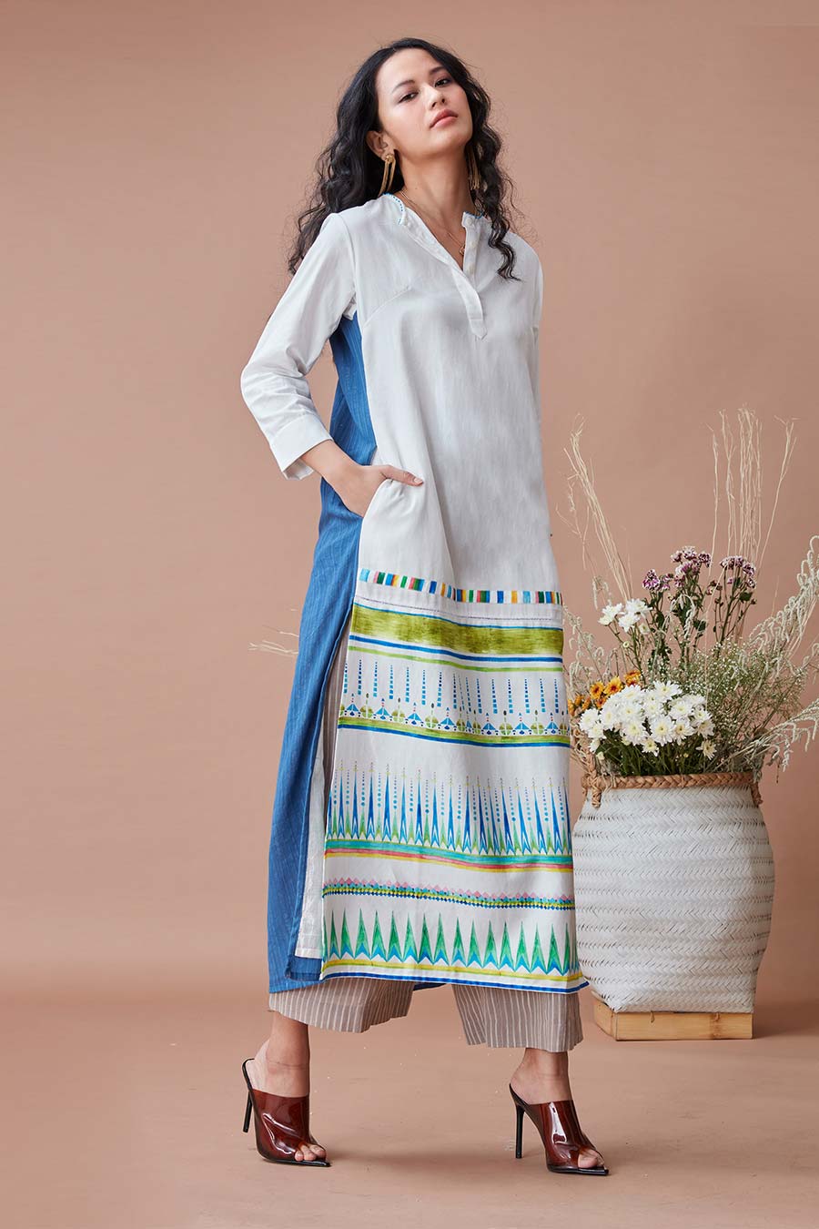 A woman wearing a white and blue kurta tunic with 3/4th sleeves, a round neck, and front button placket. The tunic has ladder lace inserts and a digitally printed panel on the front.