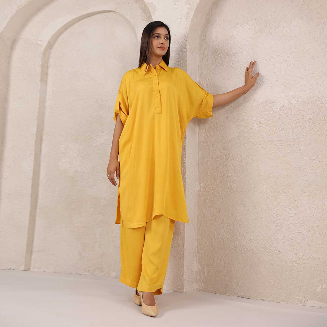 Woman in a yellow outfit standing against a textured beige wall.