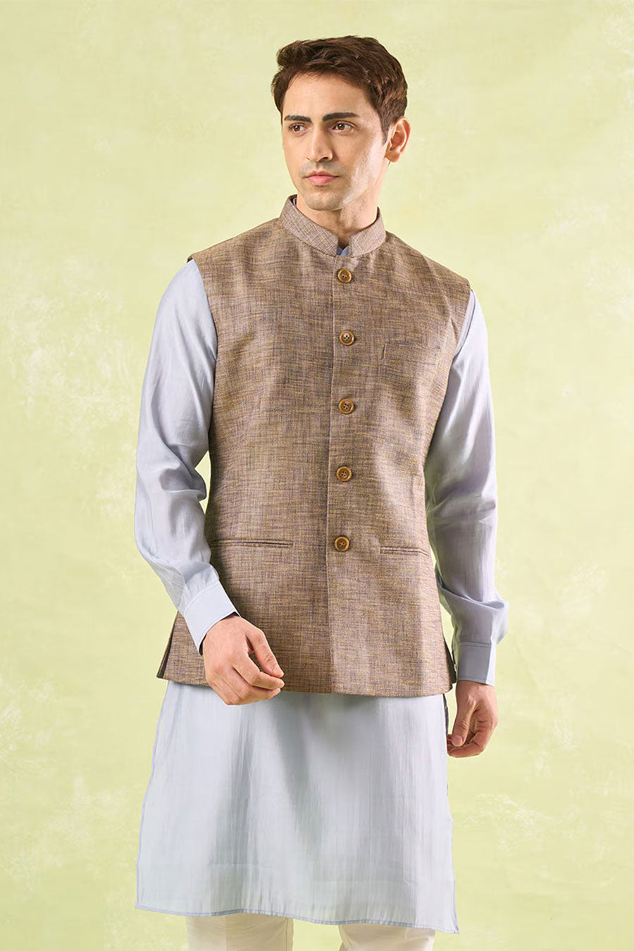 Man wearing an ethnic brown textured Bandi Nehru Jacket over a light grey shirt on a light green background