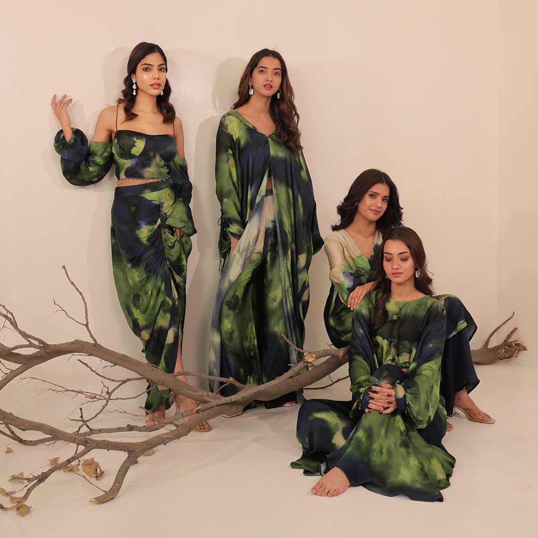 Four women in matching green and blue outfits posing with a branch against a white background