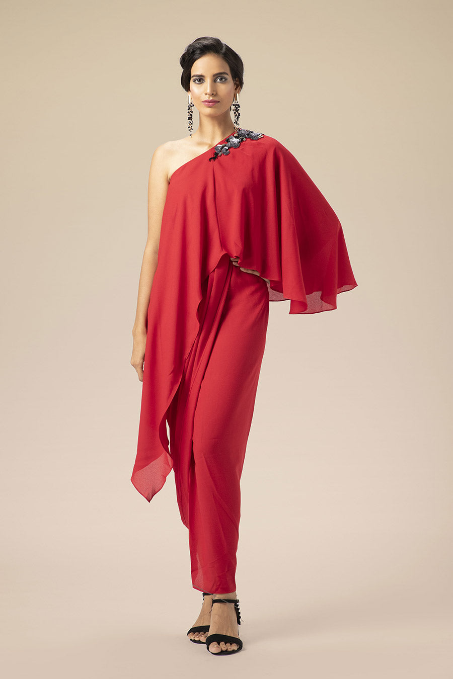 A woman modeling a one-shoulder red drape dress with cape-style overlap and hand embroidery on the shoulder.